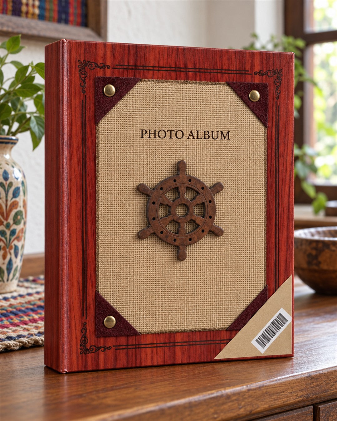 Álbum de fotos de tapa dura para 200 fotos con temática náutica: portada con acabado imitación madera caoba rojiza y marco decorativo, panel central de tela tipo yute color arena con un timón de barco de madera oscura foto del envase