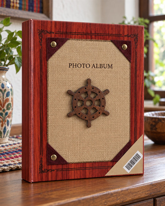 Álbum de fotos de tapa dura para 200 fotos con temática náutica: portada con acabado imitación madera caoba rojiza y marco decorativo, panel central de tela tipo yute color arena con un timón de barco de madera oscura foto del envase