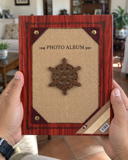 Álbum de fotos de tapa dura para 200 fotos con temática náutica: portada con acabado imitación madera caoba rojiza y marco decorativo, panel central de tela tipo yute color arena con un timón de barco de madera oscura en la mano