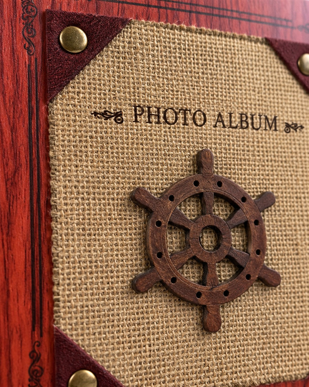 Álbum de fotos de tapa dura para 200 fotos con temática náutica: portada con acabado imitación madera caoba rojiza y marco decorativo, panel central de tela tipo yute color arena con un timón de barco de madera oscura textura y aplicación