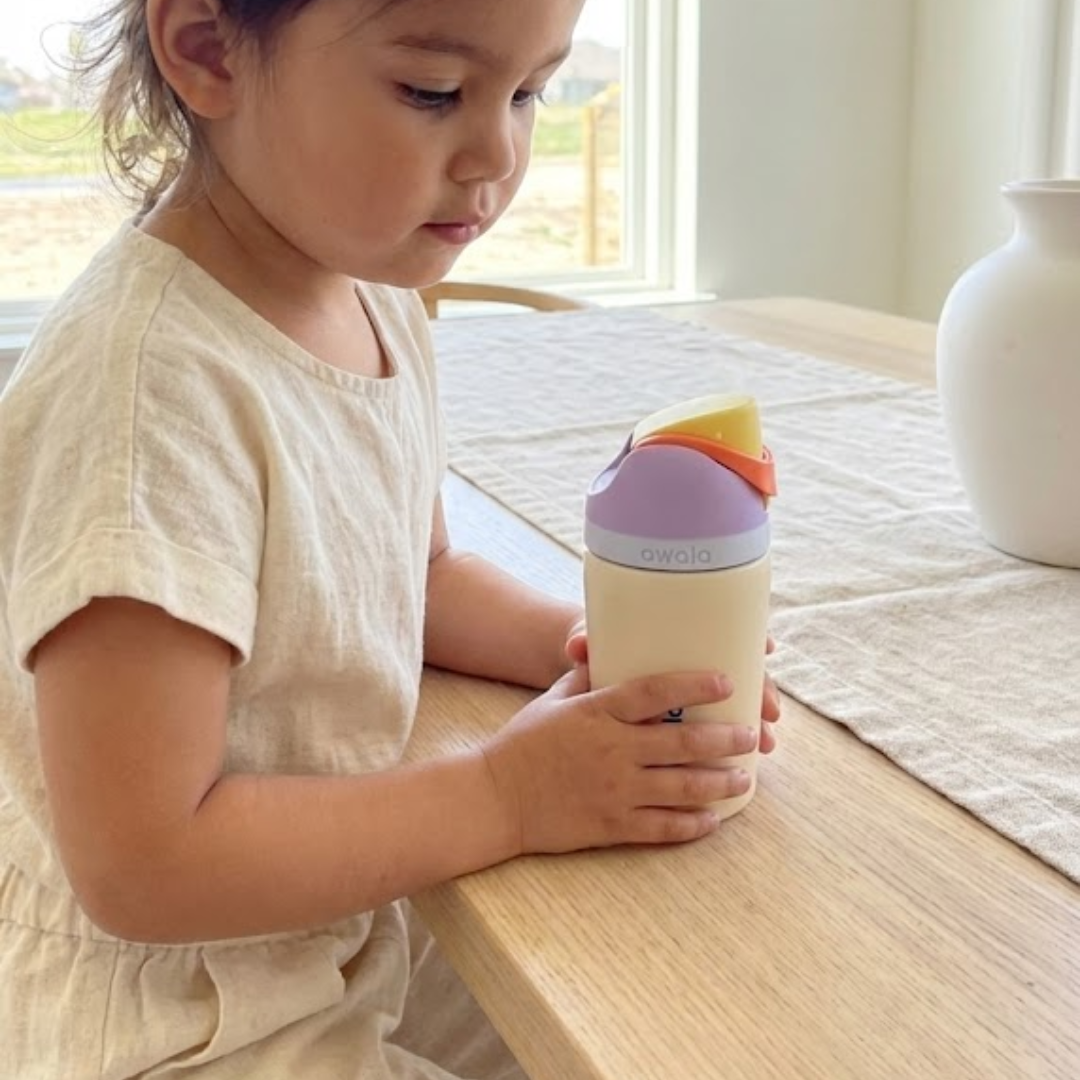 Botella térmica infantil Owala FreeSip de 12 onzas. El cuerpo del termo es color crema mate, la tapa es de color lila pastel con una banda naranja, y el botón de apertura es amarillo brillante.