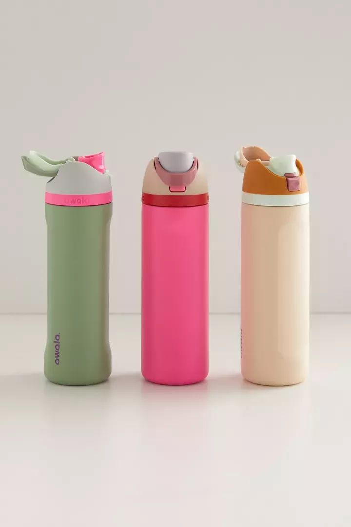 Botellas de acero inoxidable Owala FreeSip de 24 onzas. De izquierda a derecha: la primera variante (Bizarrely Bright) es de color verde olivo con una tapa gris, un aro fucsia y un botón verde menta; la segunda variante (Tropical) tiene un cuerpo fucsia vibrante con una tapa rosa pastel y un botón gris; la tercera variante (Sandy Shores) es de color beige o arena claro con una tapa ocre o café claro y un botón blanco.