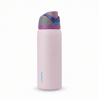 Botella térmica Owala FreeSip de 32 onzas con cuerpo en color rosado pastel. La tapa presenta una combinación armoniosa: base en color morado vibrante, cuerpo de la tapa en gris oscuro, botón en color azul cielo y el asa de seguridad en azul marino. El logotipo de Owala destaca en la parte inferior en color azul claro.