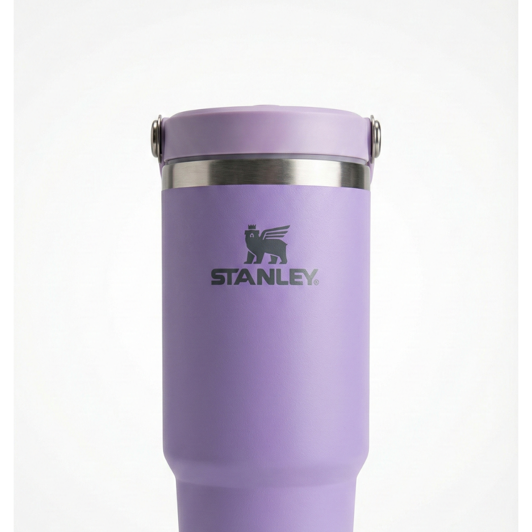 Termo de acero inoxidable de 30 onzas modelo Stanley IceFlow Flip Straw. El cuerpo es de color lila o lavanda con acabado mate. La tapa de color lila incluye una pajilla abatible integrada (flip straw) y un asa de transporte giratoria del mismo tono, con el icono del oso alado de Stanley grabado en el costado de la tapa.