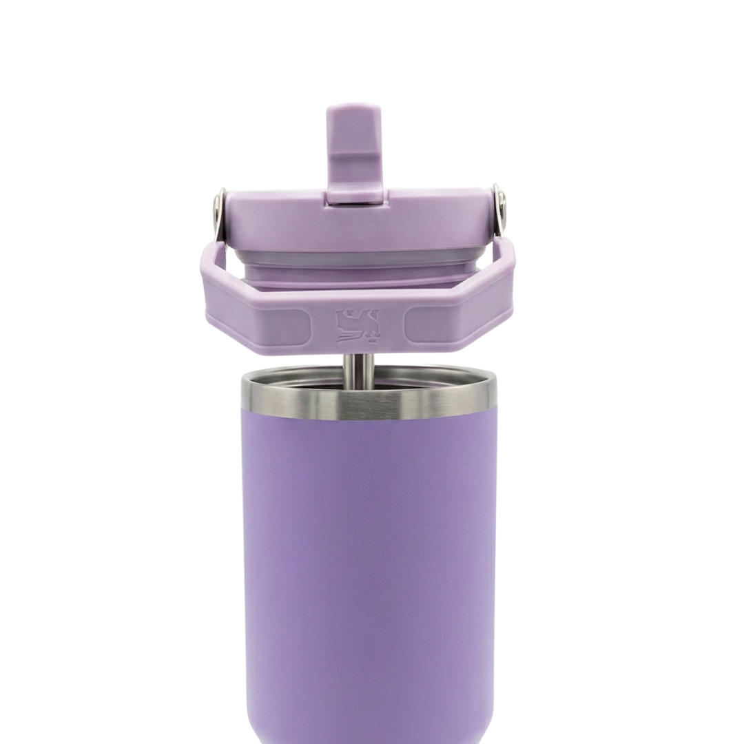 Termo de acero inoxidable de 30 onzas modelo Stanley IceFlow Flip Straw. El cuerpo es de color lila o lavanda con acabado mate. La tapa de color lila incluye una pajilla abatible integrada (flip straw) y un asa de transporte giratoria del mismo tono, con el icono del oso alado de Stanley grabado en el costado de la tapa.