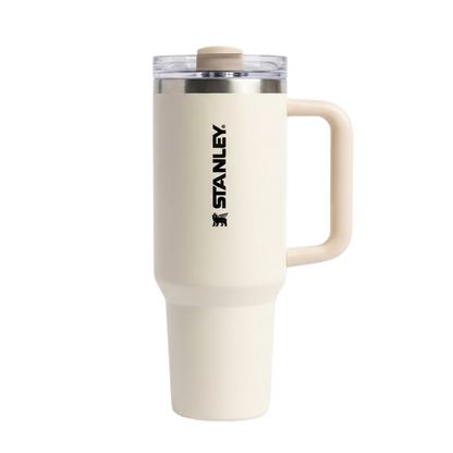 Vaso térmico de 40 onzas Stanley Quencher H2.0 en color crema o beige arena (Birch). La tapa FlowState™ presenta detalles en un tono beige ligeramente más oscuro que el cuerpo. El asa de transporte es robusta en el mismo color crema con refuerzo interno. El logotipo de Stanley destaca en color negro vertical, otorgando un aspecto minimalista y limpio.