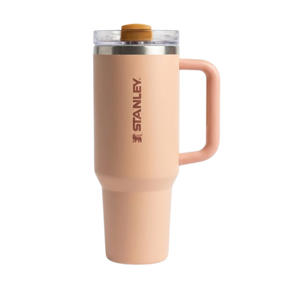 Termo Stanley Quencher H2.0 de 40 onzas en color Rose Quartz, un tono rosa pálido o arena rosada mate. Incluye asa ergonómica del mismo color, tapa transparente FlowState™ con detalles en color café claro y pajilla (popote) reutilizable. Logotipo de Stanley en color café vertical en el centro.