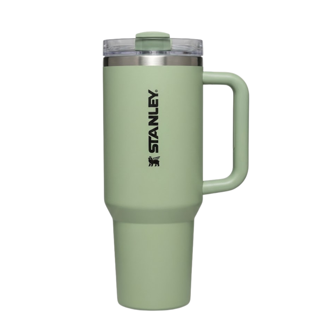 Termo Stanley Quencher H2.0 de 40 onzas en color verde salvia o verde cemento (Sage) con acabado mate. La tapa transparente tiene la pieza giratoria en color verde a juego. El asa ergonómica es de color verde con detalles en gris oscuro. Presenta el logotipo de Stanley grabado en color negro. Es un diseño de inspiración natural y moderna.