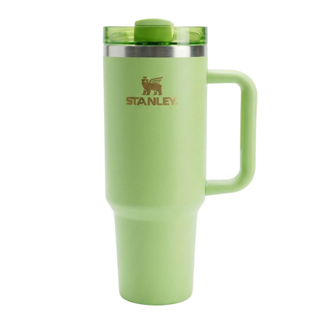 Vaso térmico Stanley de 40 onzas en color verde, perteneciente a una colaboración especial con Starbucks. En el lateral, presenta un grabado vertical elegante que dice "STANLEY + STARBUCKS" junto al icono del oso alado de Stanley, todo en un tono dorado suave o bronce. El asa y el cuerpo son del mismo tono verde lima, con una tapa transparente que tiene un cierre superior y pajilla en verde a juego.